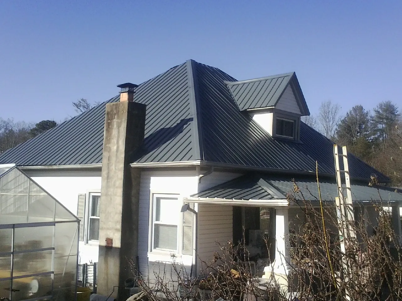 Dark blue standing seam metal roof on a white farmhouse with dormer — Slate & Tile Roof Repair by Roofing Brothers in Brush Valley