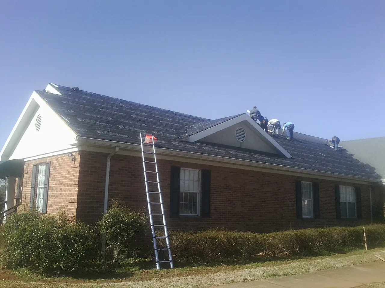 Crew tearing shingles off a brick ranch roof with a ladder set — Emergency Roof Repair work by our crew in Brush Valley