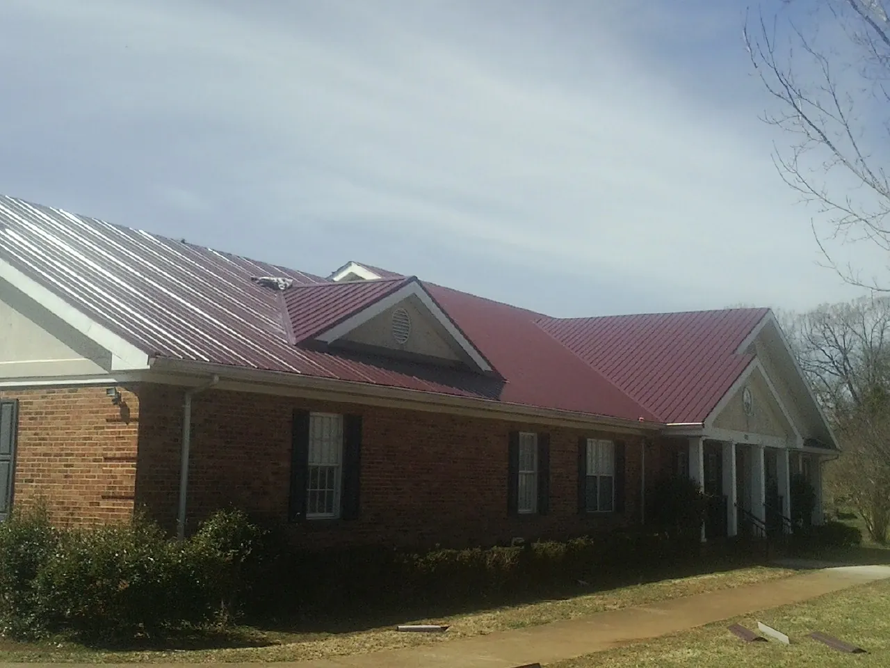 Red metal roof with gabled entries on a long brick building, from a Hail Damage Roof Repair job in Brush Valley