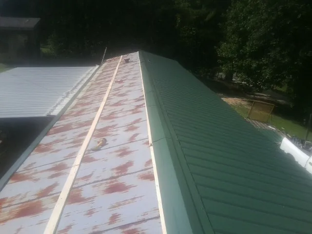 Old rusted panels beside newly installed green metal roofing — Wind Damage Roof Repair by Roofing Brothers in Brush Valley
