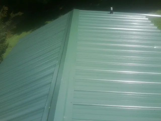 New green metal panels meeting at the ridge of a roof — Flat Roof Repair work by our crew in Brush Valley