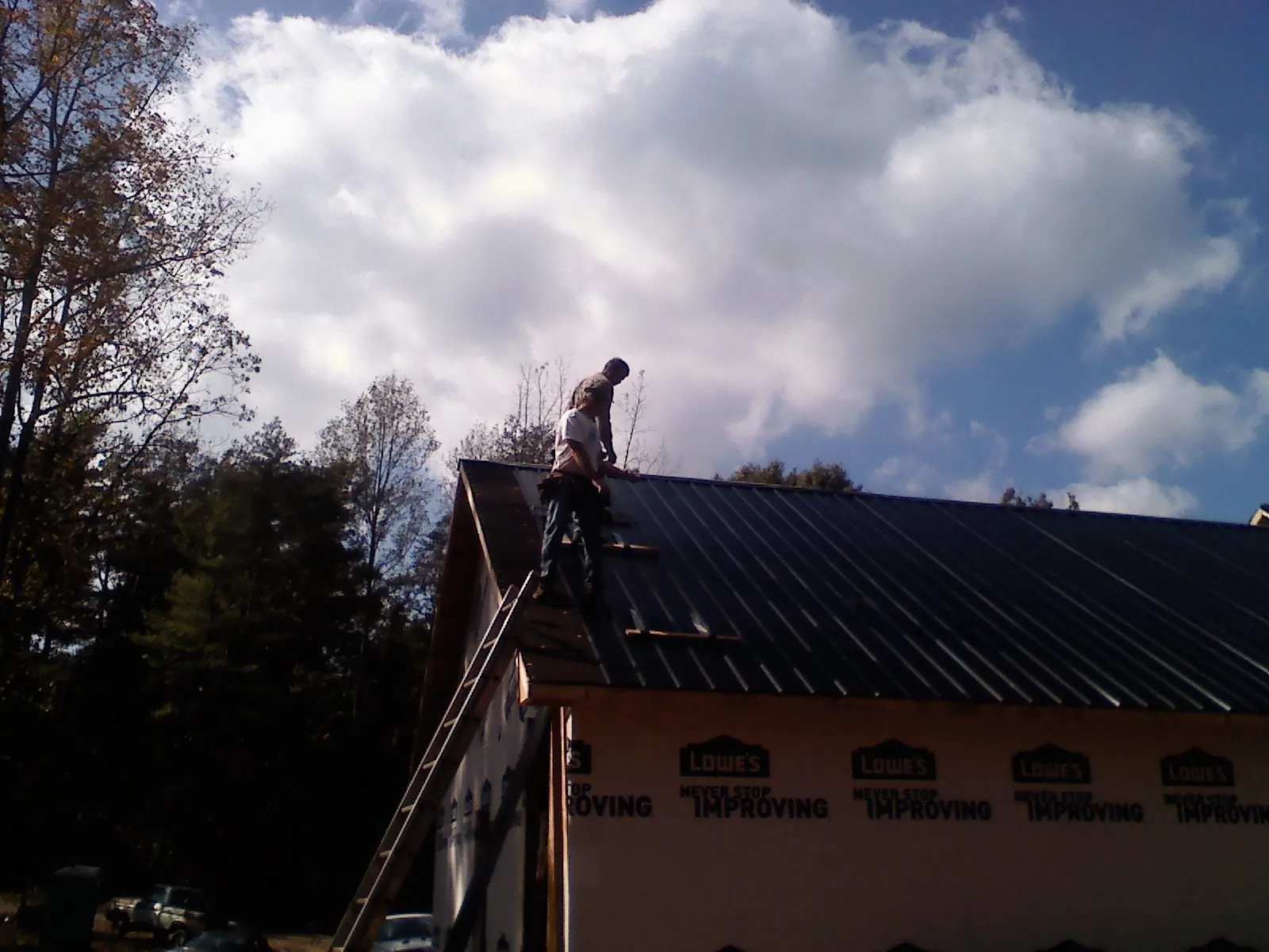 Roofer fastening dark metal panels high against a cloudy sky, from a Roof Inspection job in Brush Valley