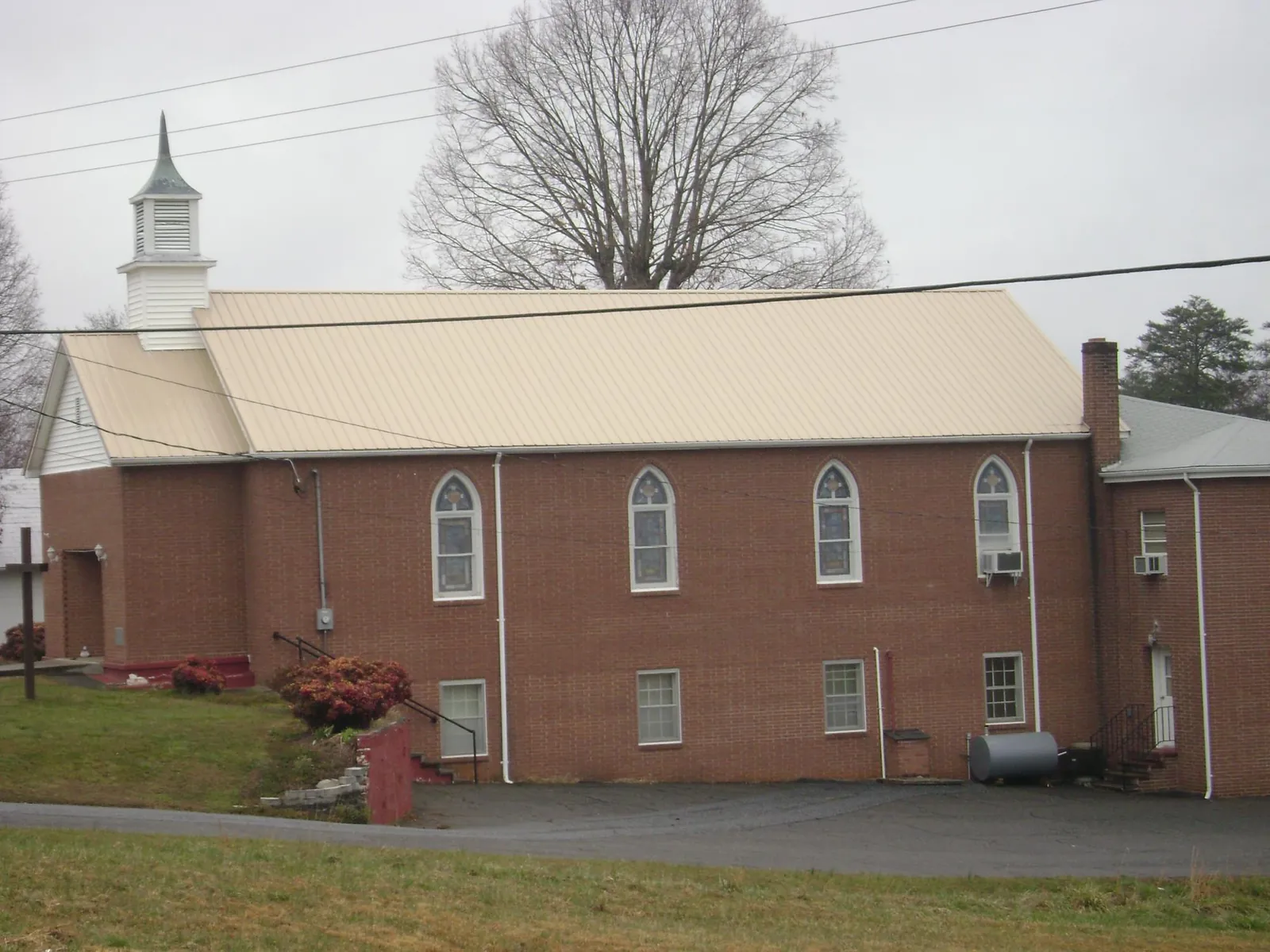 New tan metal roof on a brick church with a white steeple in Brush Valley