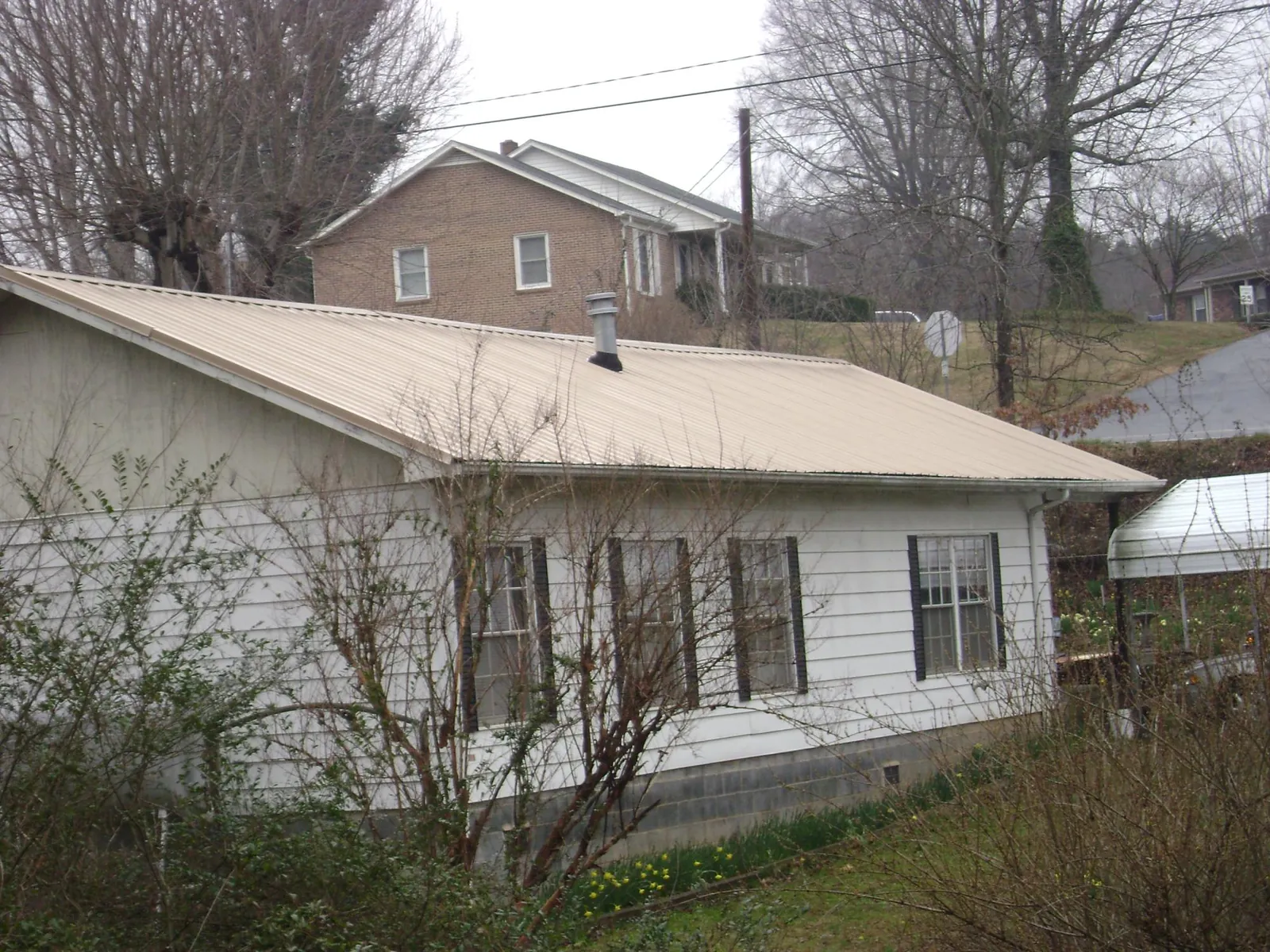 Tan metal roof on a white sided house set into a hillside — Commercial Roofing by Roofing Brothers in Brush Valley